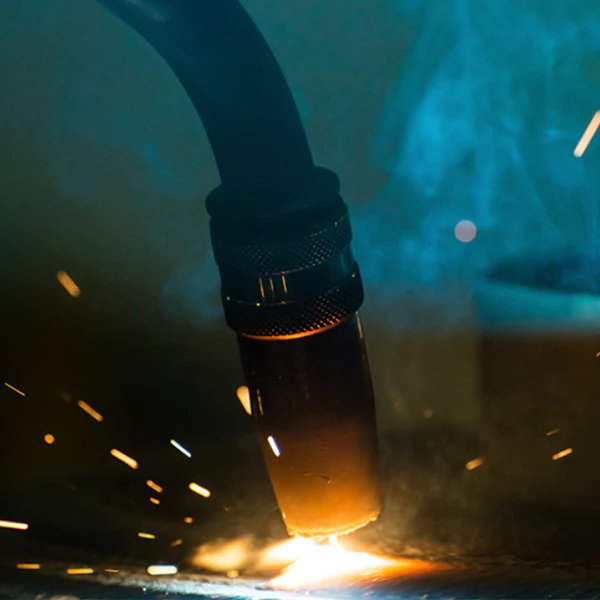 Image of a torch head with a cup attached welding onto a piece of metal