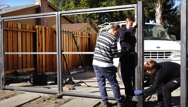 Image of three men putting up a metal gate in the driveway