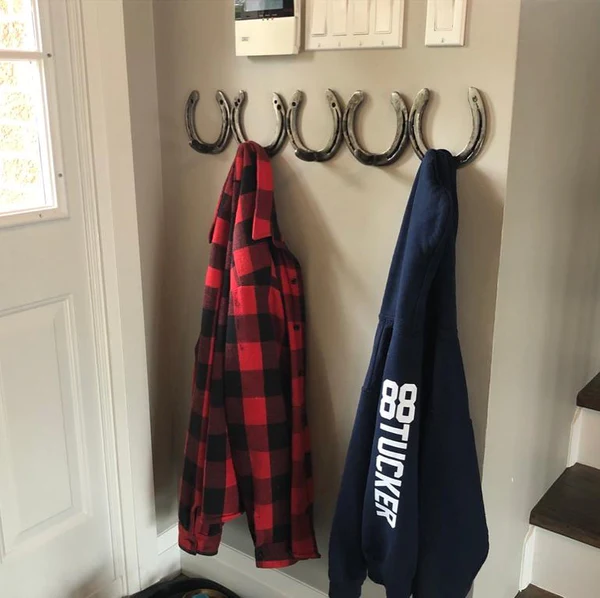 Image of four horseshoes mounted to a wall with two coats hanging from two of them