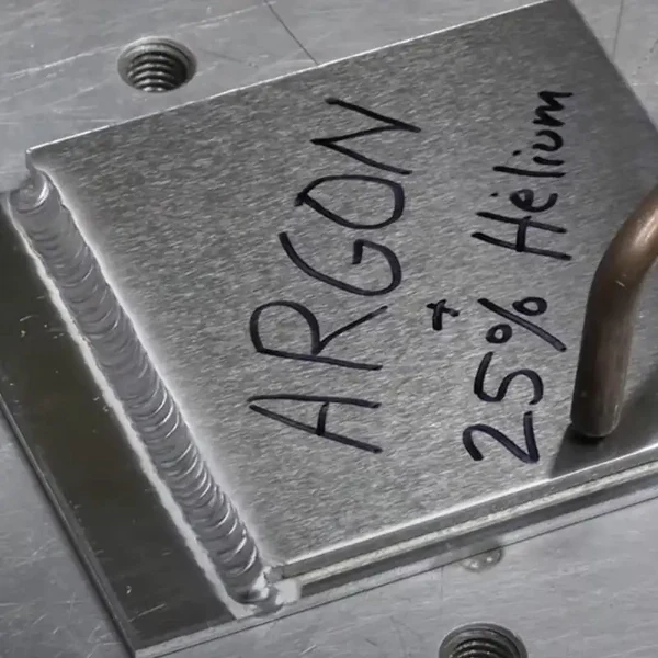 Image of a metal sheet that has been welded on the left-hand side with the argon and helium gas values written on the top of the sheet