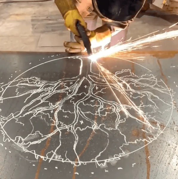 Image of a welder using a plasma cutter to create a metal piece of art